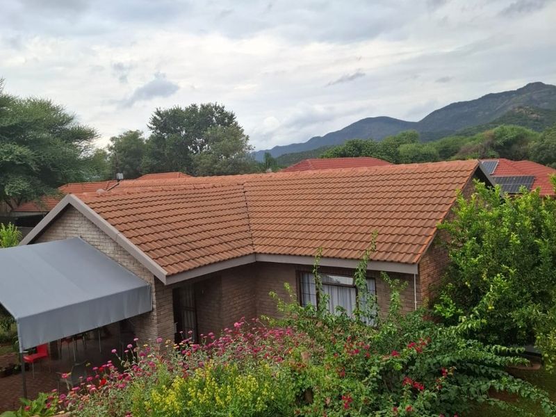 Elevated view of a brick house featuring a terracotta tiled roof, a covered patio area, and a well-maintained garden with mountain views.