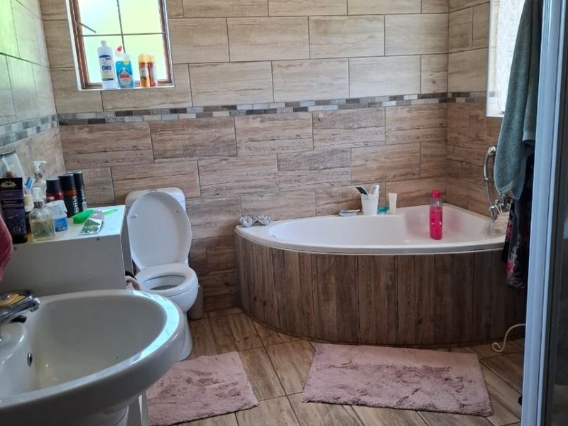 A functional bathroom featuring a corner bathtub, pedestal basin, toilet, and shower enclosure with wood-look wall and floor tiling.