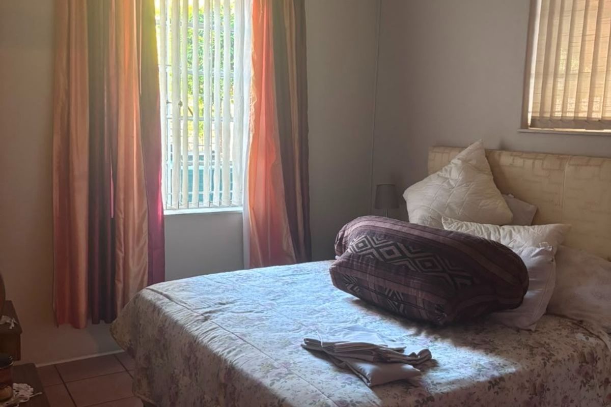 A functional bedroom featuring tiled flooring, vertical blinds, and a wall-mounted air conditioning unit.
