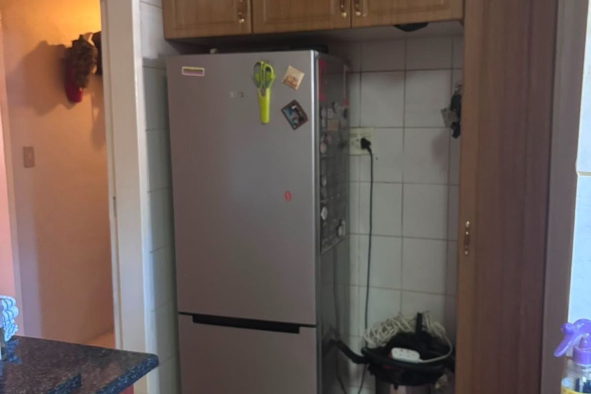 A functional kitchen area featuring built-in wooden cabinetry, tiled splashbacks, and durable tiled flooring, providing practical storage and workspace.
