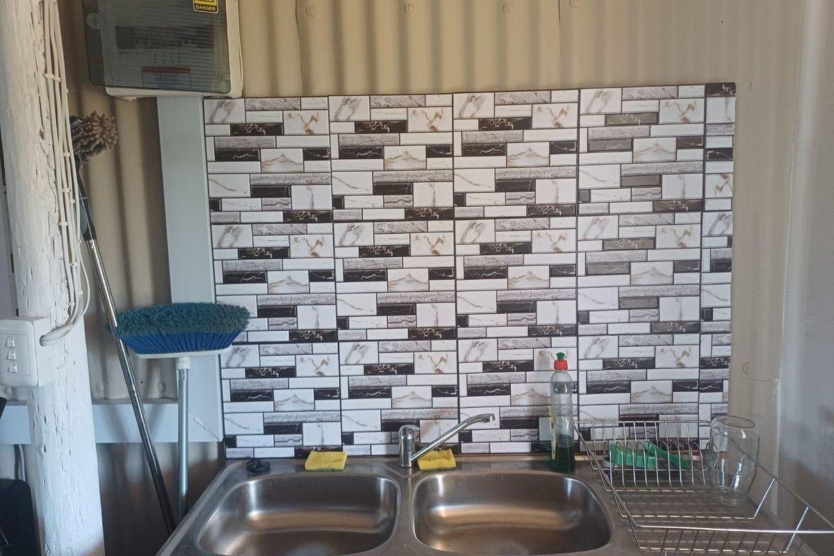 A functional kitchen sink area featuring a double stainless steel basin, mixer tap, and decorative tiled splashback against corrugated metal wall cladding.