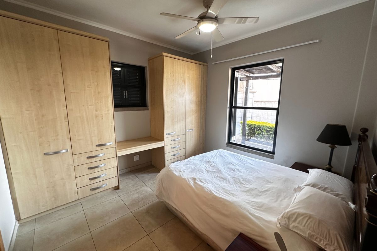 A well-maintained bedroom featuring built-in light wood cabinetry, an integrated desk, tiled flooring, and a ceiling fan.
