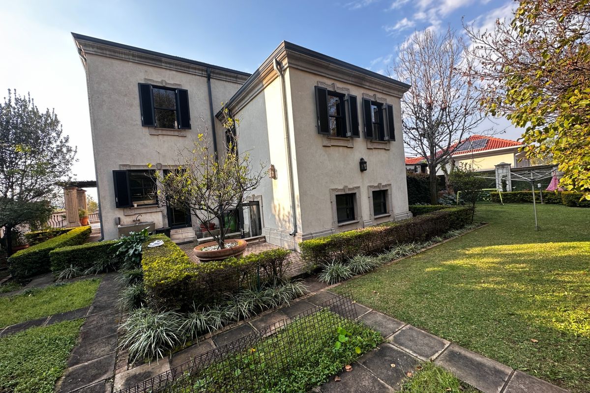 A well-maintained rear exterior view of the house featuring a stone-paved patio, landscaped garden with hedging, and classic window shutters.