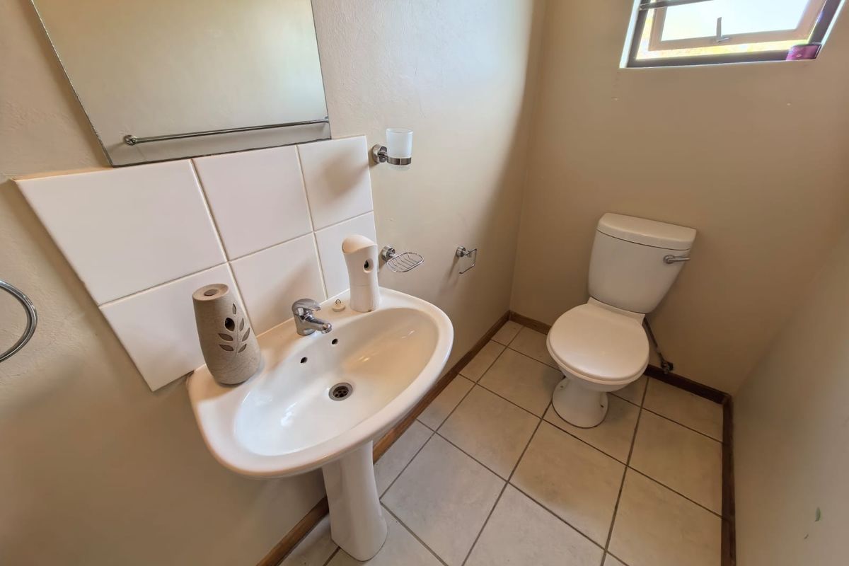 A functional guest bathroom featuring a pedestal basin, ceramic toilet, tiled splashback, and neutral floor tiles with natural light from a top-hung window.