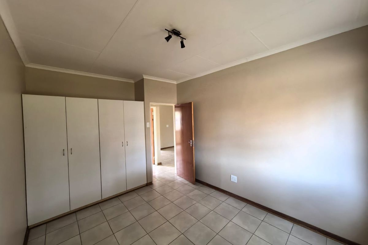 A clean, empty bedroom featuring neutral wall paint, tiled flooring, and ample built-in cupboard storage space.