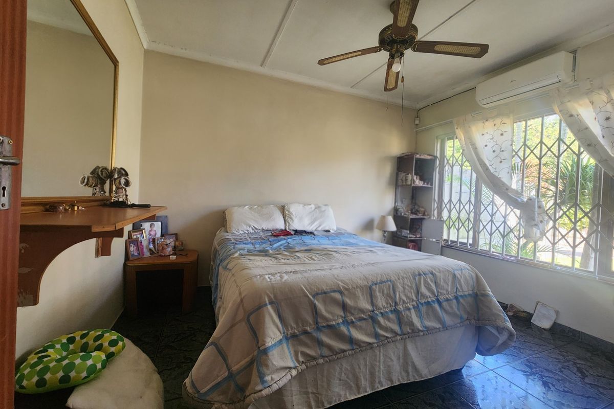 A bedroom featuring tiled flooring, a ceiling fan, and a wall-mounted air conditioning unit, with security bars installed on the window.