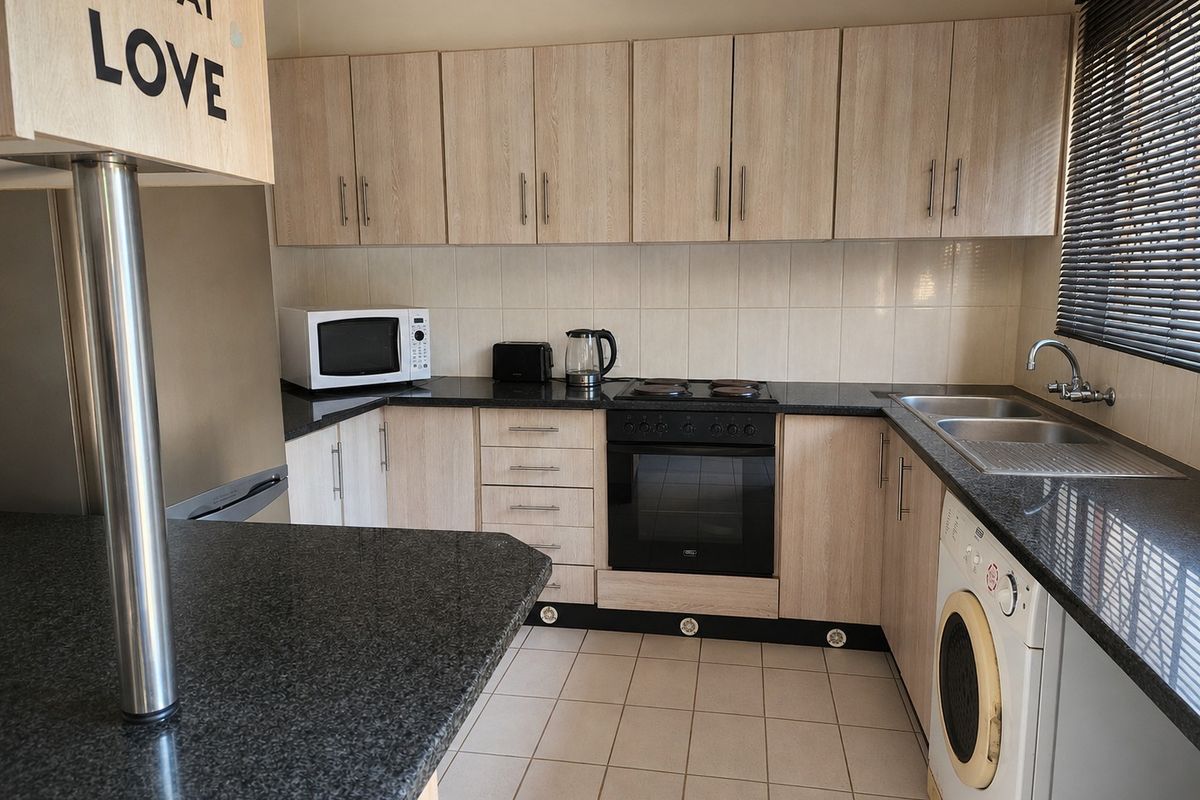 A functional kitchen featuring light wood-grain cabinetry, dark granite countertops, built-in oven and hob, and a double bowl sink with tiled finishes.