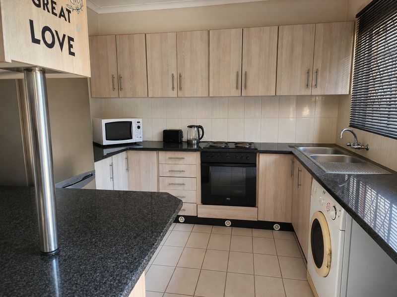 A functional kitchen featuring light wood-grain cabinetry, dark granite countertops, built-in oven and hob, and a double bowl sink with tiled finishes.