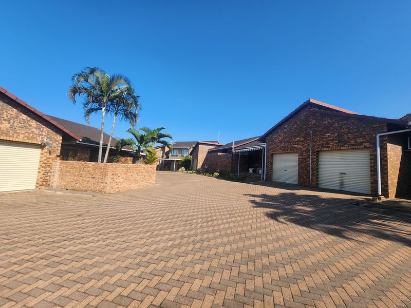 A view of the townhouse complex exterior featuring brick facades, multiple garage doors, and a well-maintained paved driveway.