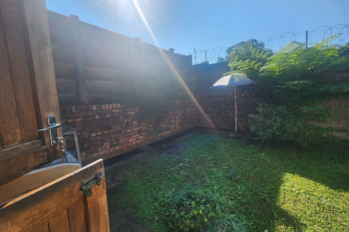 A private rear garden area featuring a brick boundary wall with security fencing and a small lawn space.