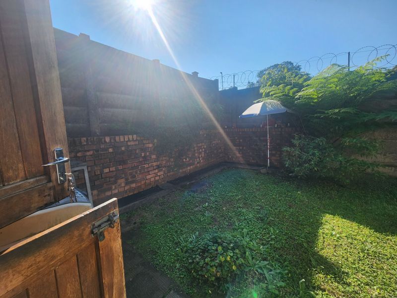 A private rear garden area featuring a brick boundary wall with security fencing and a small lawn space.