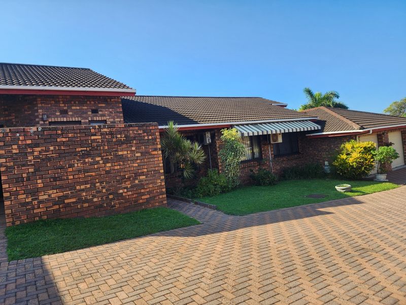 Front view of a face brick townhouse featuring a paved driveway, tiled roof, and a retractable awning over the window.