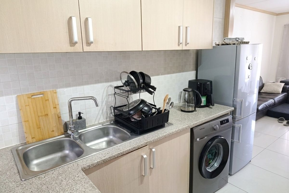 A functional kitchen featuring light wood-look cabinetry, a granite-effect countertop, tiled backsplash, and an integrated washing machine.