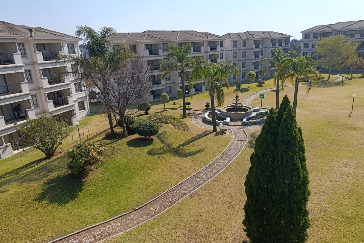 Elevated view of a well-maintained communal garden area featuring a central stone fountain, paved walkways, and surrounding multi-story apartment buildings.
