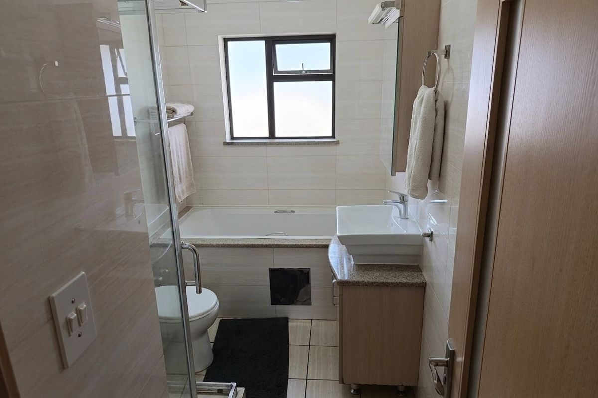 A functional bathroom featuring a built-in bathtub, a glass-enclosed shower, and a vanity with a vessel sink, finished with neutral wall and floor tiles.