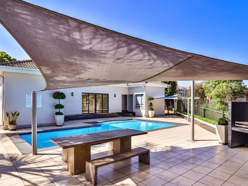 Outdoor pool area featuring a tiled patio, shade sail, and built-in braai, perfect for entertaining and relaxation.