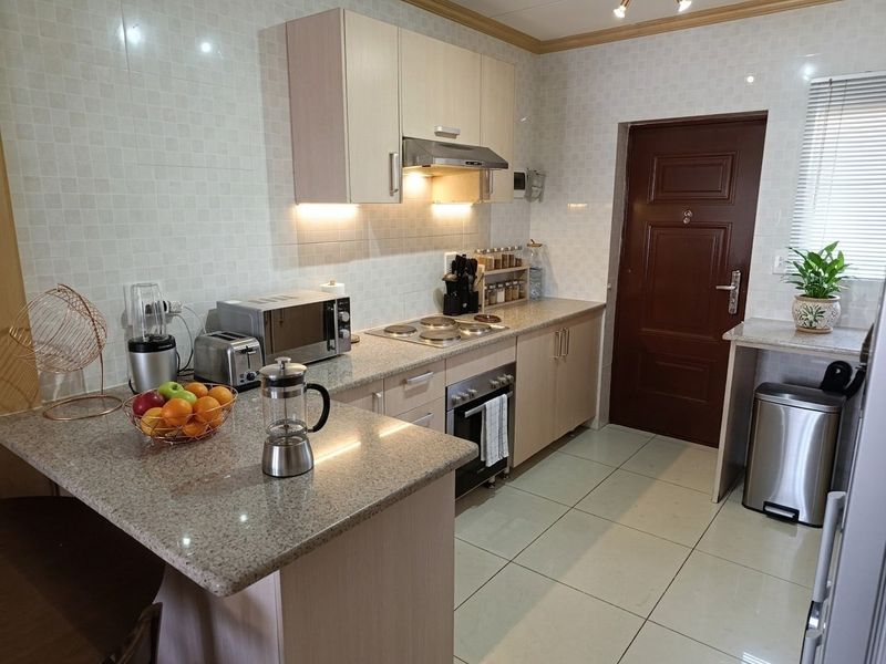 A functional kitchen featuring granite countertops, built-in cabinetry, an electric hob with extractor fan, and tiled finishes throughout.