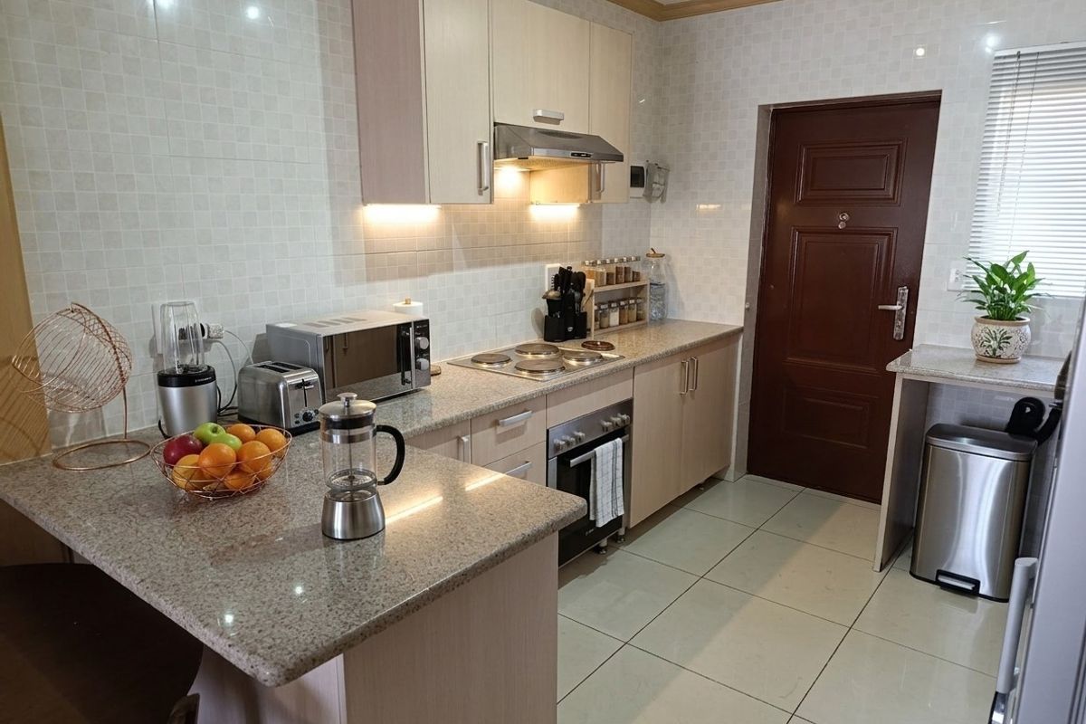 A functional kitchen featuring granite countertops, built-in cabinetry, an electric hob with extractor fan, and tiled finishes throughout.