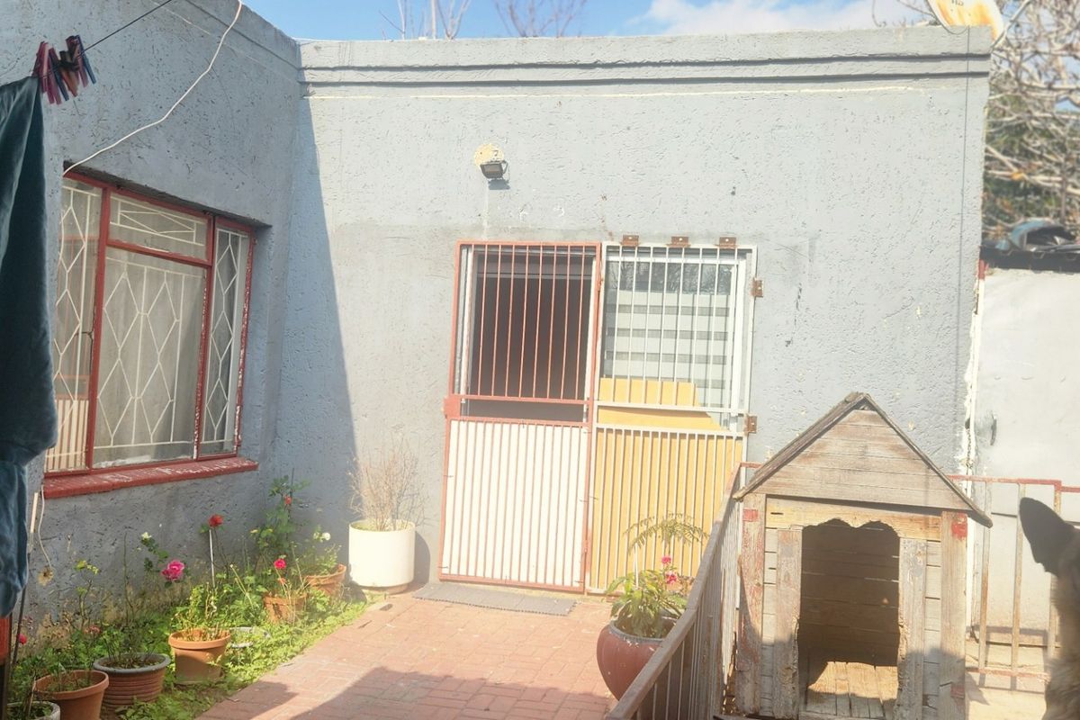 Rear exterior view of the property featuring a paved walkway, security gate, and textured wall finish.