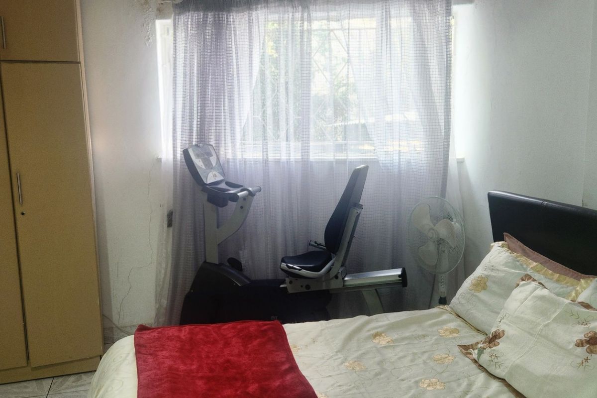 A bedroom featuring built-in cupboards and security bars on the window, showing signs of wear and wall cracking.