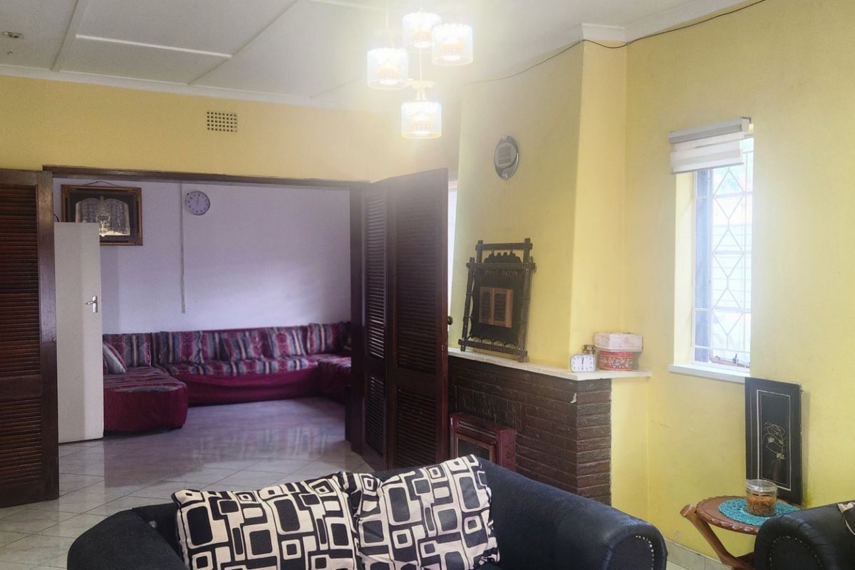 A living room featuring a brick fireplace, tiled flooring, and louvered double doors leading to an adjacent living space.