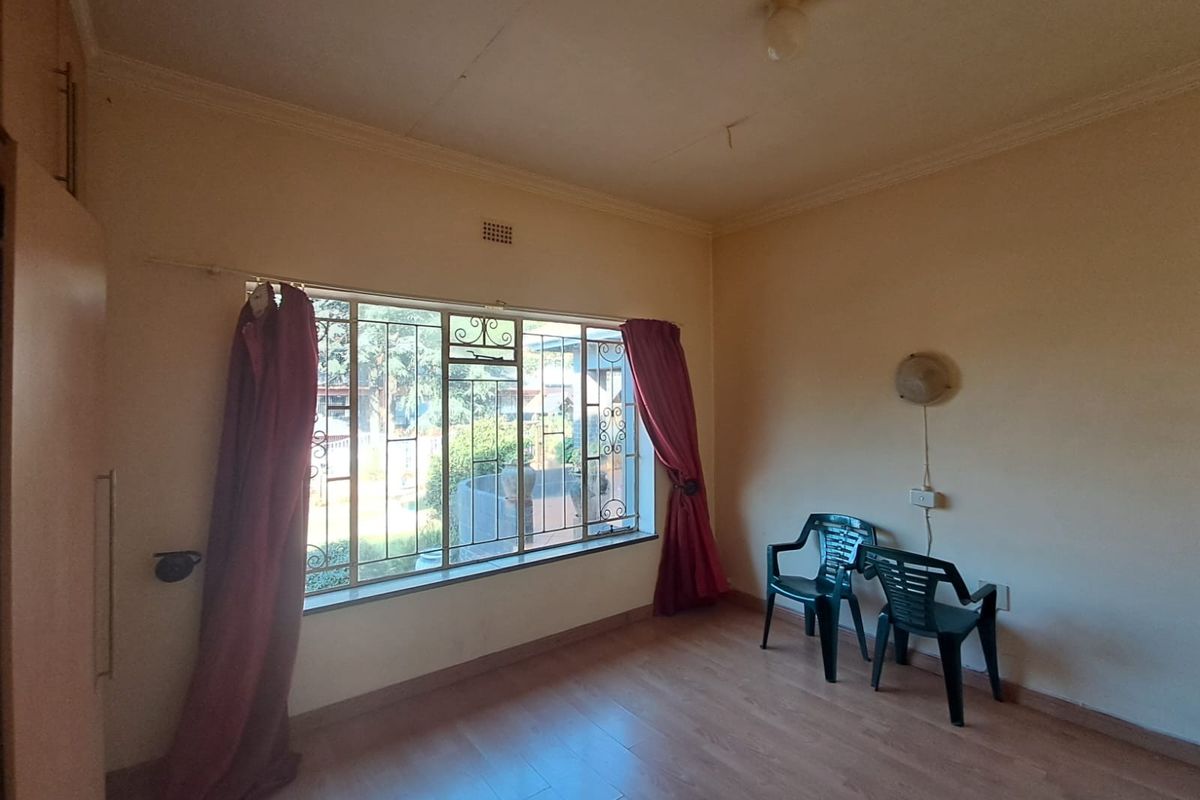 A bedroom featuring laminate flooring, built-in cupboards, and security bars on the window. The room requires cosmetic updates to the ceiling and walls.