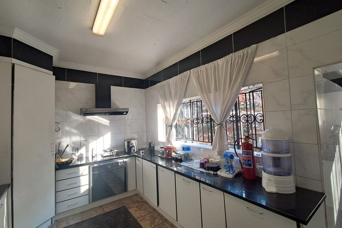 A functional kitchen featuring white cabinetry, dark granite countertops, built-in oven and hob, and tiled splashbacks with security bars on the window.