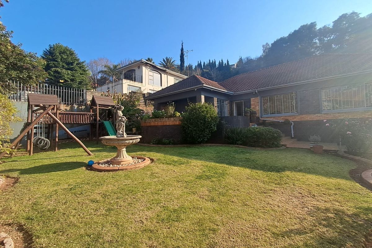 A well-maintained rear garden featuring a lawn, brick retaining wall, and a classic stone fountain, set against the rear elevation of the house.