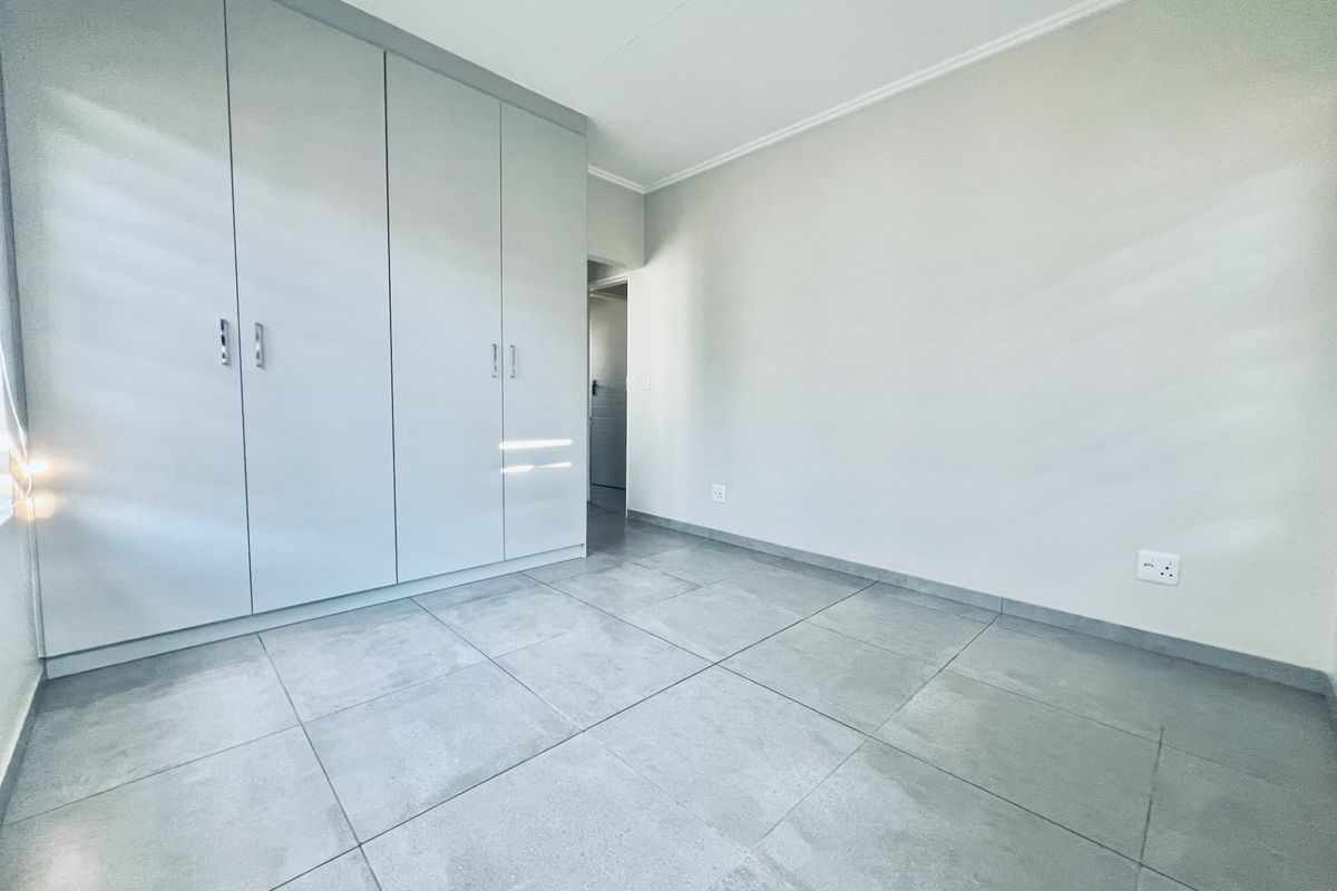 A bright, empty bedroom featuring modern grey floor tiles and ample built-in cupboard storage space.