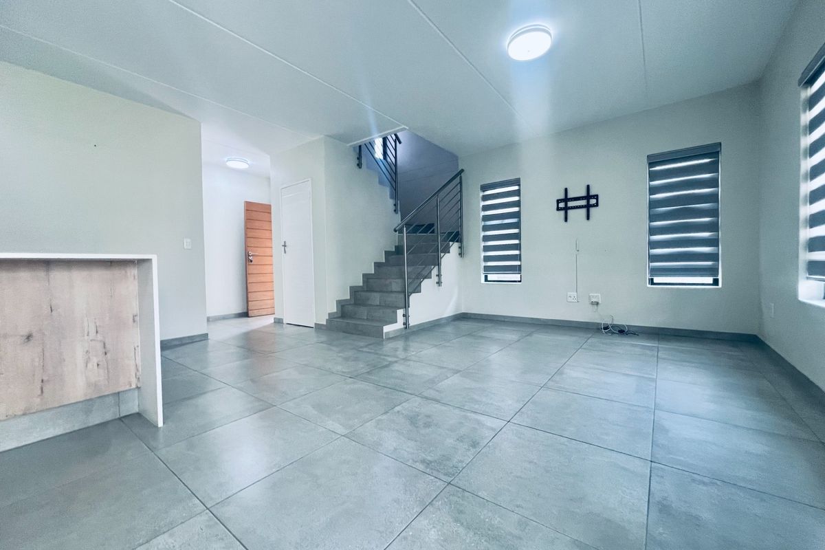 Spacious open-plan living area featuring large format floor tiles, a modern staircase with metal balustrade, and neutral finishes throughout.