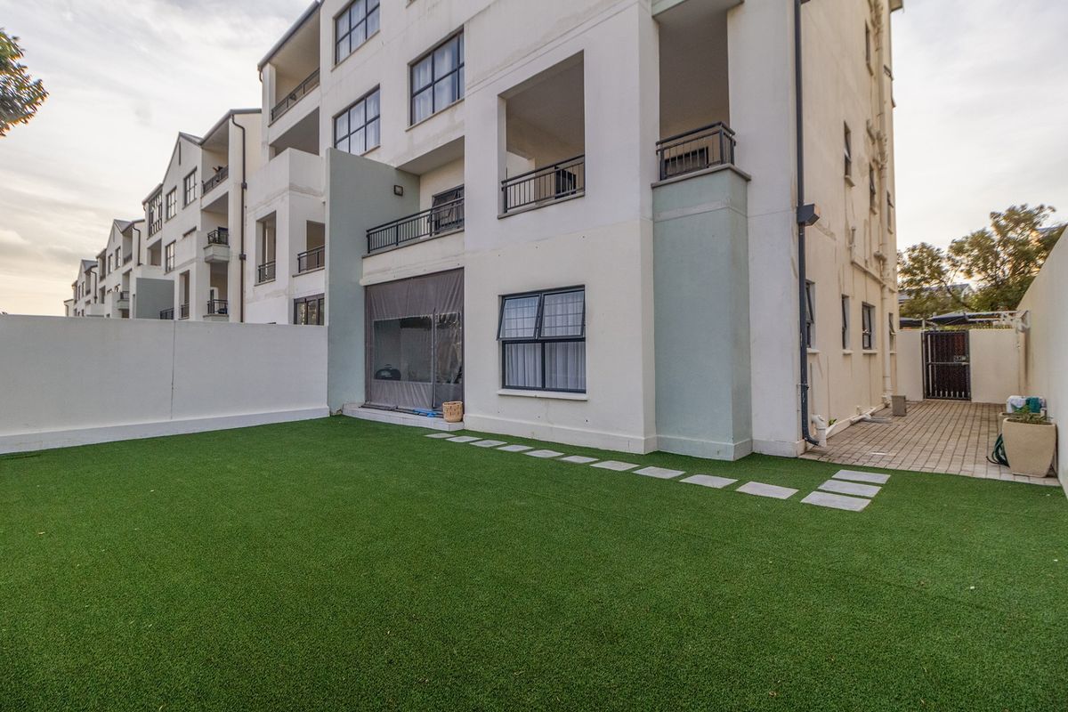 A well-maintained rear exterior view of an apartment complex featuring a private artificial lawn, paved patio area, and multiple balconies.