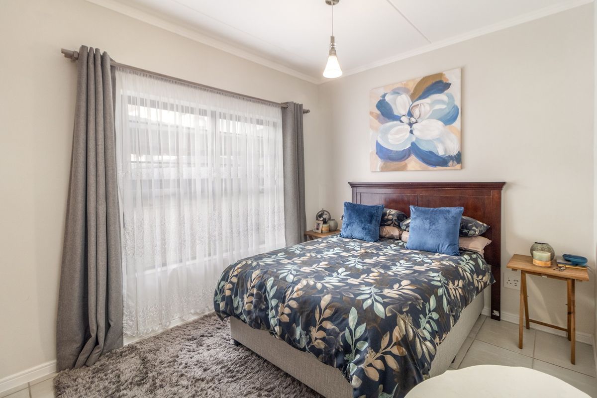 A well-maintained bedroom featuring neutral wall tones, tiled flooring, and a large window with installed curtain rods and sheer drapes.