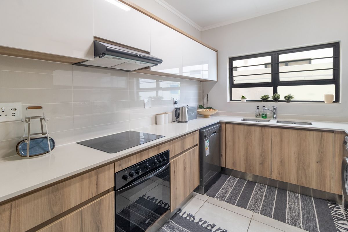 Modern kitchen featuring sleek wood-grain and white cabinetry, stone countertops, integrated appliances, and a tiled backsplash with a functional double basin sink.
