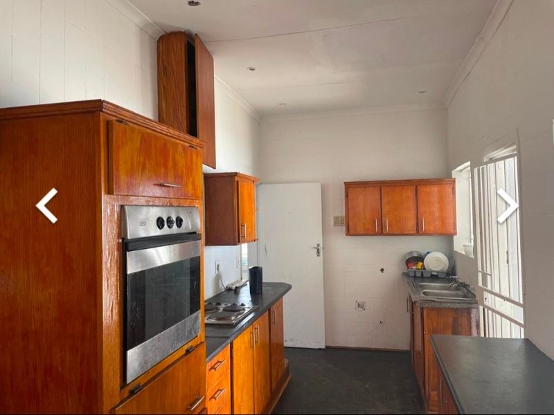 A dated kitchen featuring wooden cabinetry, built-in oven, hob, and double sink, requiring cosmetic updates to modernize the space.