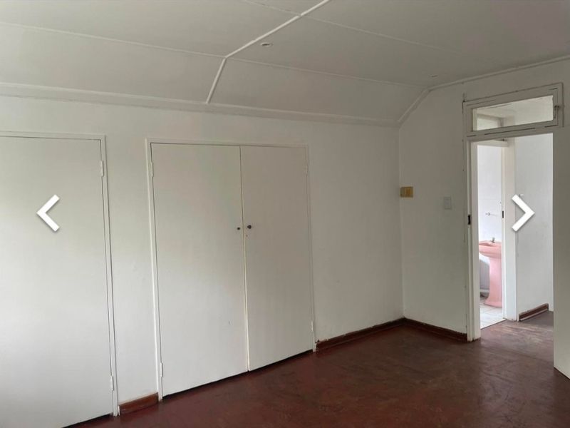 An empty bedroom featuring built-in cupboards and original timber flooring, with a doorway leading to an adjacent bathroom.