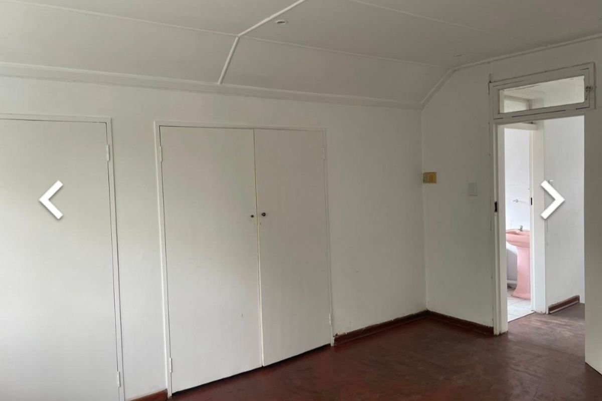 An empty bedroom featuring built-in cupboards and original timber flooring, with a doorway leading to an adjacent bathroom.
