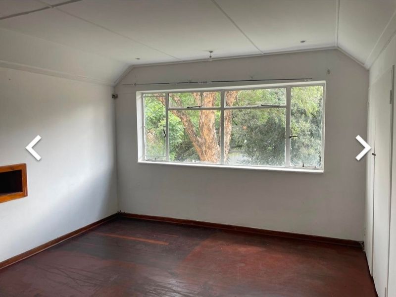 A vacant bedroom featuring original timber flooring, a large window with garden views, and a built-in wall niche.