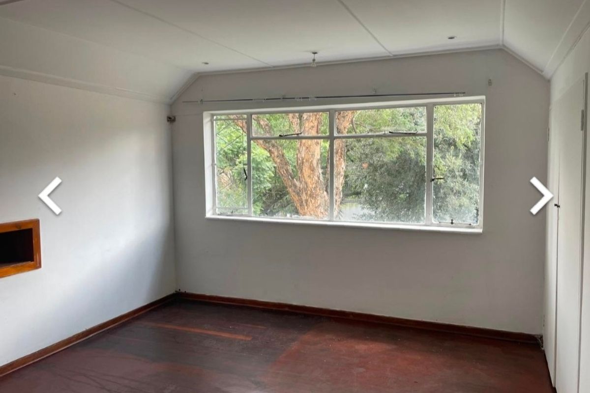 A vacant bedroom featuring original timber flooring, a large window with garden views, and a built-in wall niche.