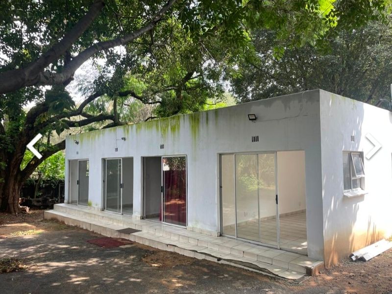 Exterior view of a detached structure featuring multiple sliding glass doors, a tiled patio area, and visible signs of exterior wall weathering and maintenance needs.