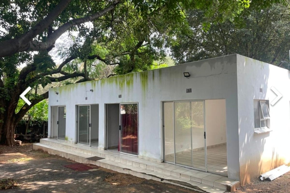 Exterior view of a detached structure featuring multiple sliding glass doors, a tiled patio area, and visible signs of exterior wall weathering and maintenance needs.