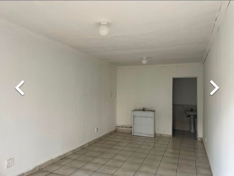 An empty open-plan living area featuring tiled flooring, a small sink cabinet, and an adjacent room with a pedestal basin.