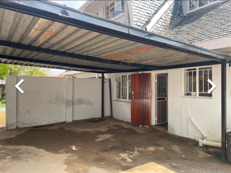 A covered carport area featuring a corrugated metal roof, concrete flooring, and direct access to the main dwelling via a timber door and security gate.
