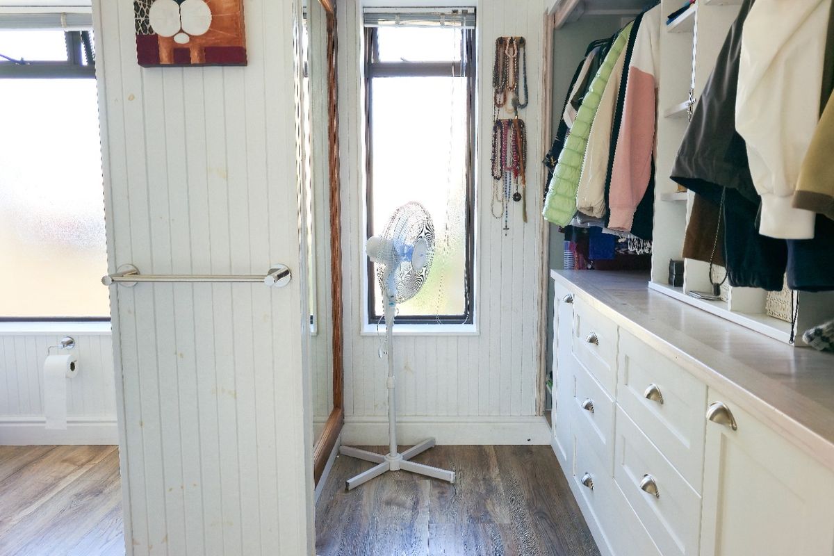 A combined bathroom and dressing area featuring built-in cabinetry, beadboard wall paneling, and a toilet, with wood-look laminate flooring throughout.