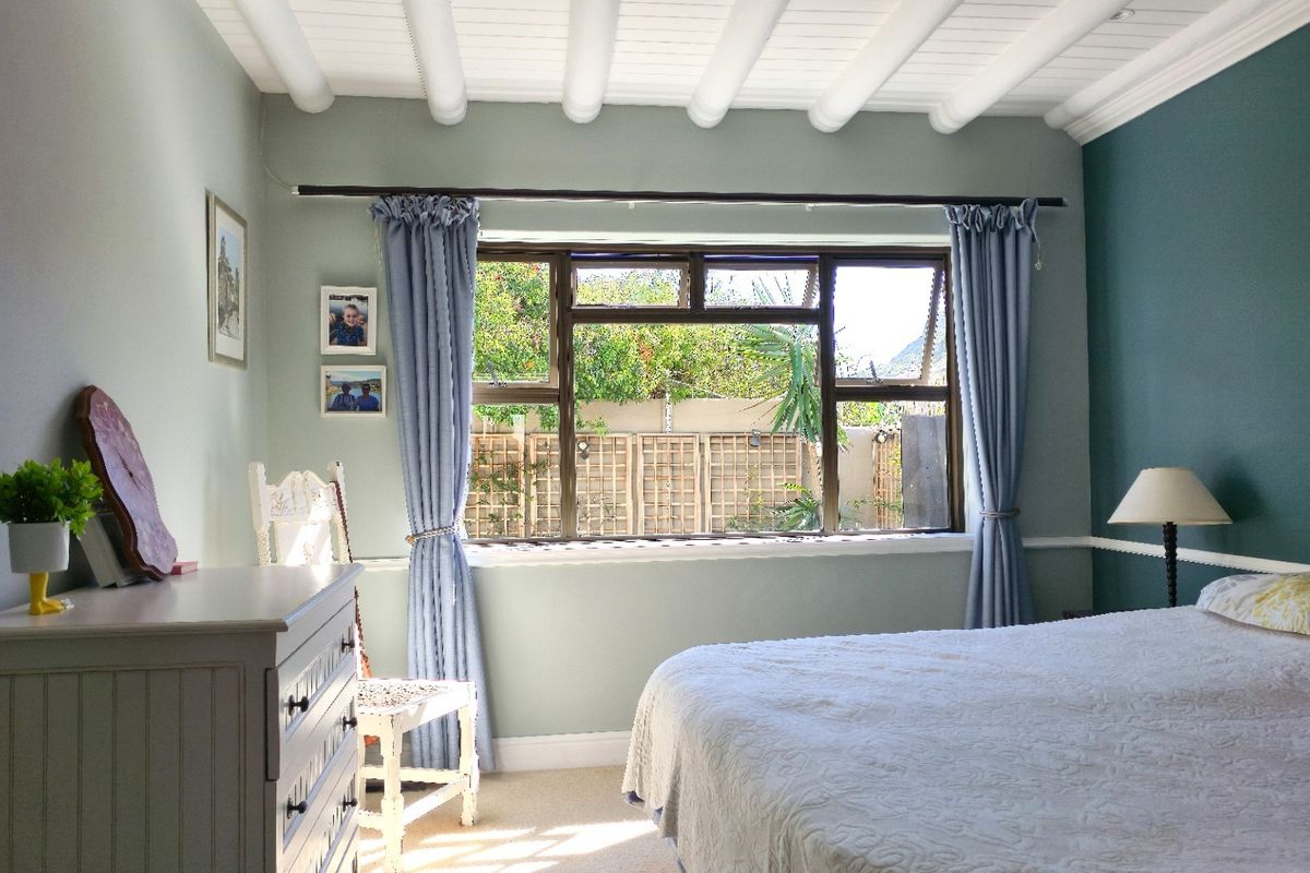 A well-maintained bedroom featuring exposed beam ceilings, a chair rail, and a large casement window overlooking the garden.