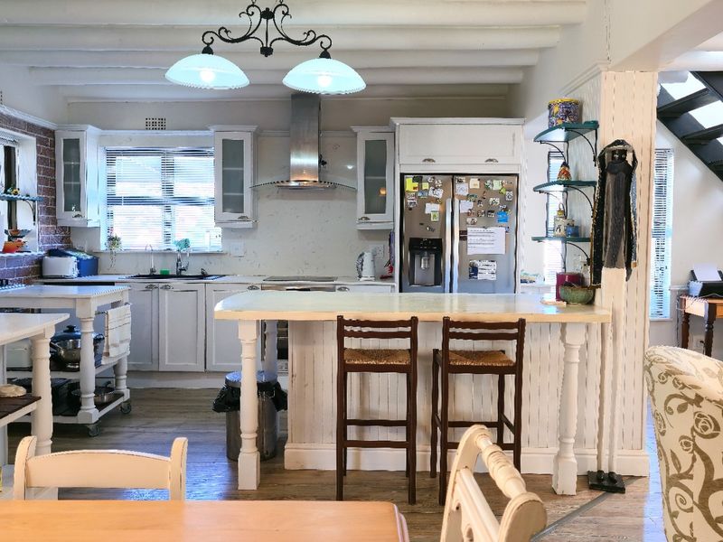 Open-plan kitchen featuring white cabinetry, a central island, exposed ceiling beams, and an adjacent staircase, creating a bright and functional living space.