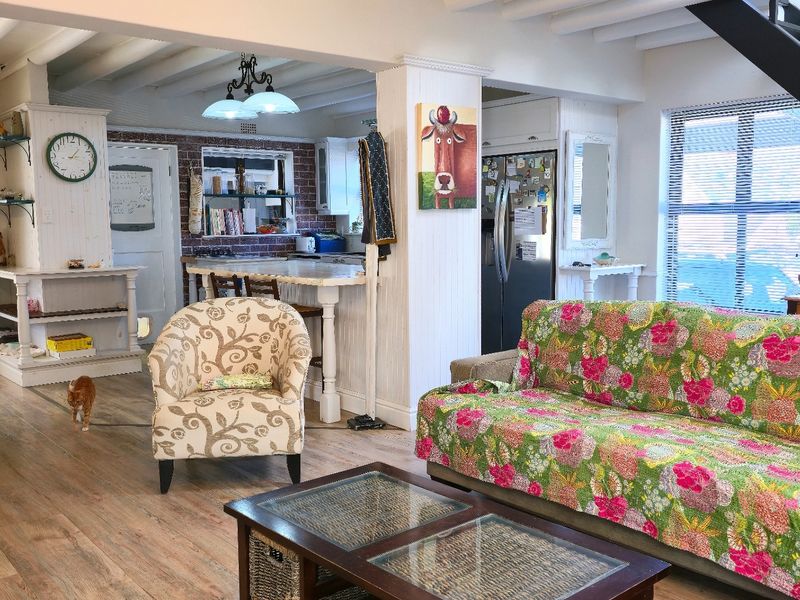 Open-plan living and kitchen area featuring exposed beam ceilings, a brick feature wall, and a central kitchen island with a staircase.