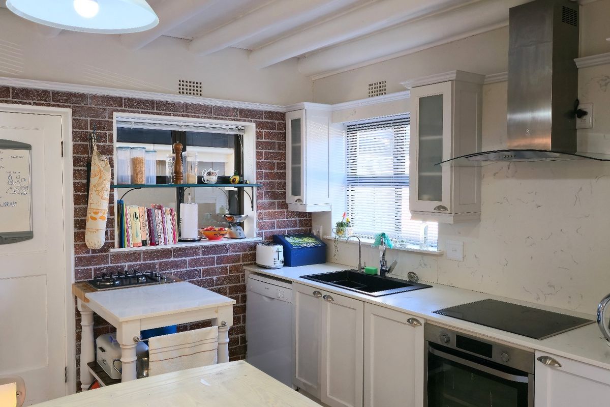 A charming kitchen featuring exposed brick walls, shaker-style cabinetry, stainless steel appliances, and exposed ceiling beams, offering a blend of rustic and modern elements.