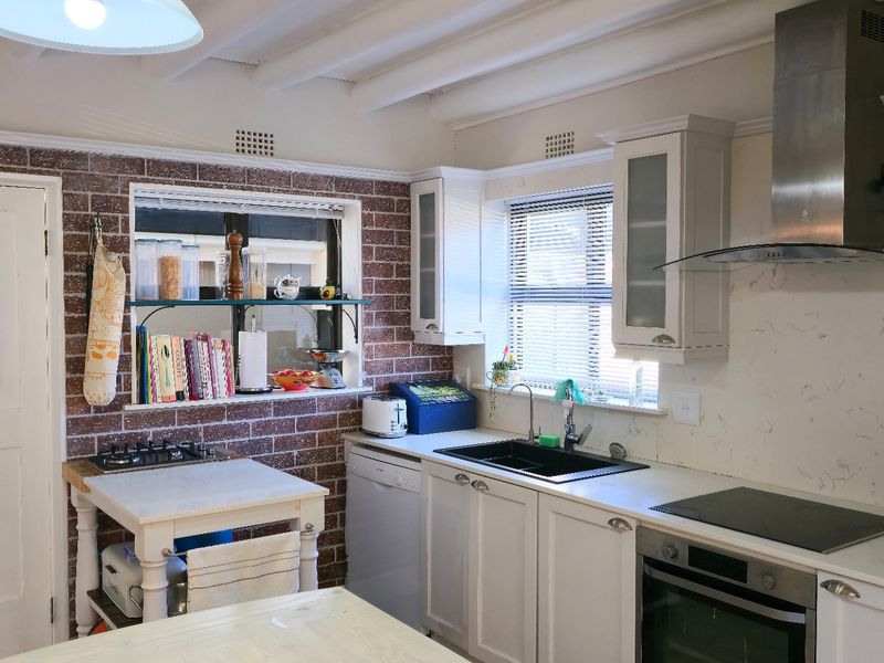 A charming kitchen featuring exposed brick walls, shaker-style cabinetry, stainless steel appliances, and exposed ceiling beams, offering a blend of rustic and modern elements.