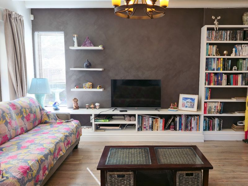 A cozy living room featuring a dark feature wall, built-in media console, integrated shelving, and warm laminate flooring.