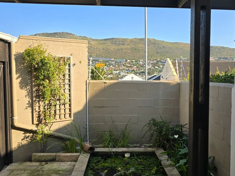 A covered patio area featuring a built-in pond, paved flooring, and a trellis, offering scenic mountain and neighbourhood views.
